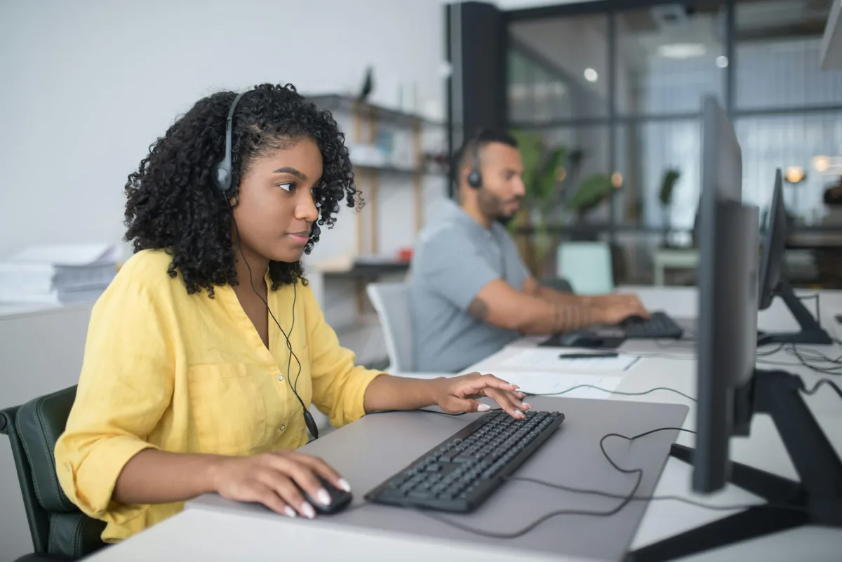 Two people working on their computers, with headsets on, in a modern office setting