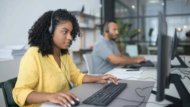 Two people working on their computers, with headsets on, in a modern office setting
